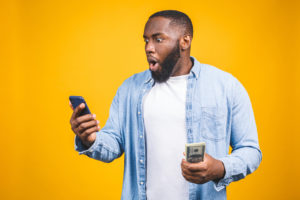 Man holding cash looking at his phone surprised